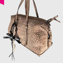 Cromia Bow Taschenanhänger aus schwarzem Leder mit heller Gliederkette, Schleife und Zahlenschloss an beiger Tasche