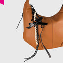 Cromia Bow Taschenanhänger aus Leder mit Kette, Schleife und Schlüsselanhänger an brauner Ledertasche befestigt